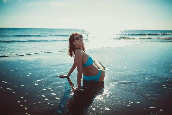 Mulher morena bonita sentada na praia de areia e sorrindo, se divertindo nas férias à beira-mar, curtindo o verão, tomando sol na costa da praia — Fotografia de Stock