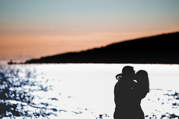 Silhouet van een paar verliefd op het strand bij zonsondergang. Het verhaal van de liefde. Man en een vrouw aan het strand. Mooie paar in het zonlicht. Silhouetten kussen tegen de zon — Stockfoto