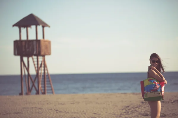 Aantrekkelijke brunette vrouw met zonnebril grappige cartoon zomer draagtas op het strand — Stockfoto