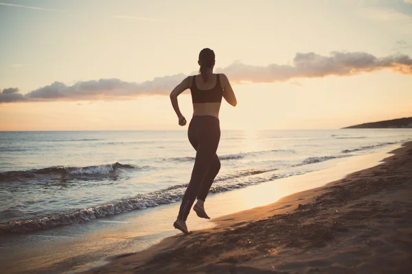 Fitness kvinna körs vid solnedgången på stranden. Aktiv passar kvinnliga fitness kvinna utbildning och arbeta ut utanför på sommaren som en del av sund livsstil livsstil — Stockfoto