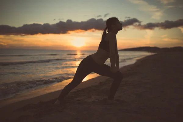 Läuferin macht Dehnübungen bei Sonnenuntergang am Strand.junge, fitte, gesunde Frau praktiziert Yoga und Pilates — Stockfoto