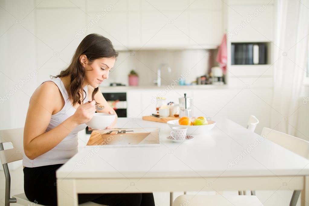 Young brunette is reading the newspaper while having breakfast at home.Modern woman lifestyle-healthy fitness breakfast,coffee and fruit,reading motivational quotes
