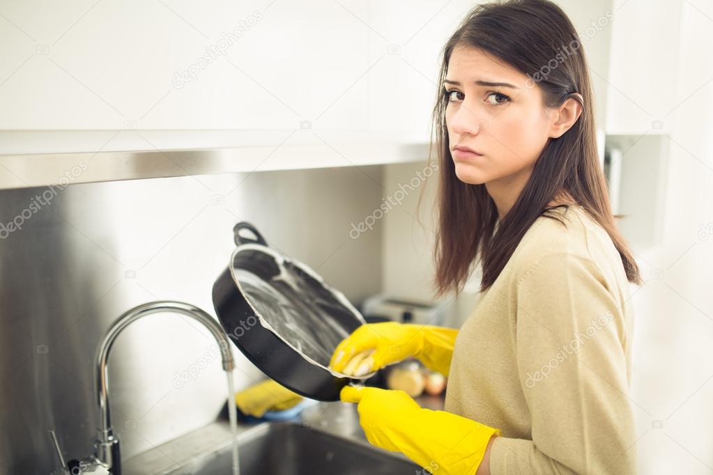 Hand cleaning.Young housewife woman washing dishes in kitchen.Tired of cleaning,making a sad face