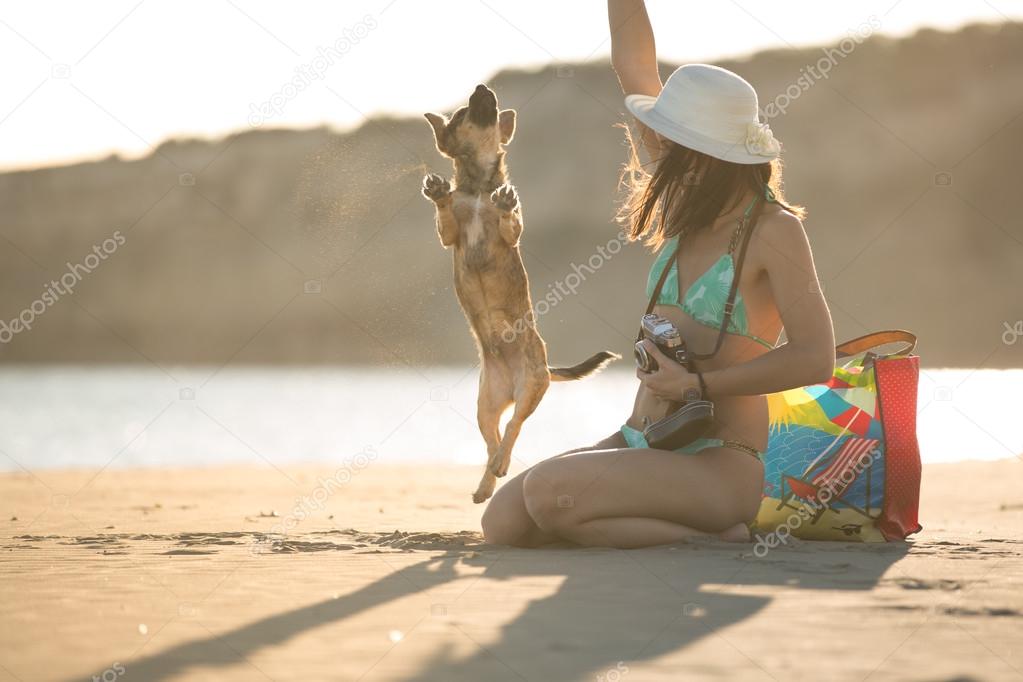 Young woman playing with dog pet on beach during sunrise or sunset.Hipster girl and dog having fun on seaside.Cute neglected stay dog adopted by caring young woman