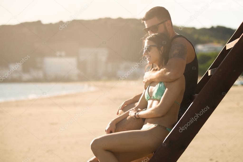 Romantic couple in hug watching sunrise/ sunset together.Young man and woman in love hugging and enjoying day at the beach.Flirting on summer vacation.Watching horizon,waves