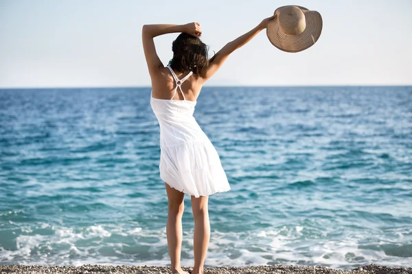 年轻漂亮的性感棕褐色的女人穿着帽子和优雅的礼服站在海滩上 风飘扬的头发 旅行和度假 欲望概念 — 图库照片