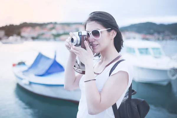 Summer hipster beach woman fun holding vintage retro camera laughing and smiling happy during summer holiday vacation travel.Women sitting on sea deck near marine boat