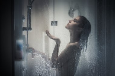 Relief and relaxation after long stressful day.Taking moment for yourself concept.Skincare,spa and aromatherapy.Unfocused portrait of a woman showering through the bath screen with little drops