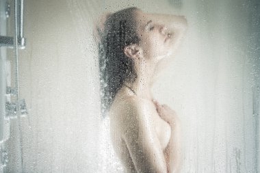 Relief and relaxation after long stressful day.Taking moment for yourself concept.Skincare,spa and aromatherapy.Unfocused portrait of a woman showering through the bath screen with little drops