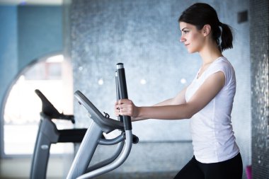 Fitness girl is working out with stepper.Strong brunette with curly hair doing aerobics on stepper.Strong young girl exercising on stepper.Woman doing fitness exercises on stepper at gymnasium