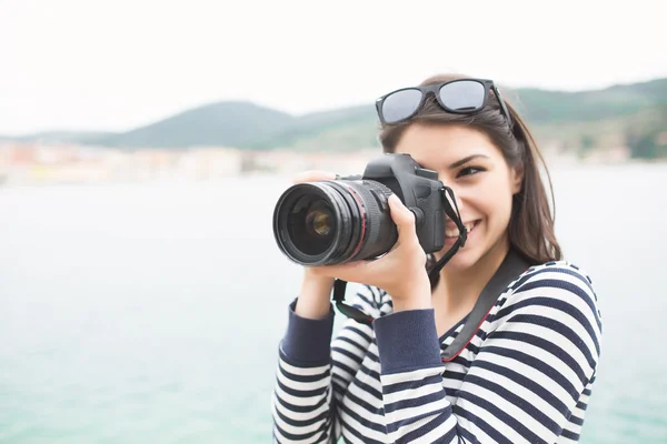 Femme heureuse en vacances photographier avec un appareil photo dslr sur la plage et souriant. — Photo