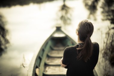Girl at the old fishing boat looking to the lake.Melancholia sadness sorrow concept.