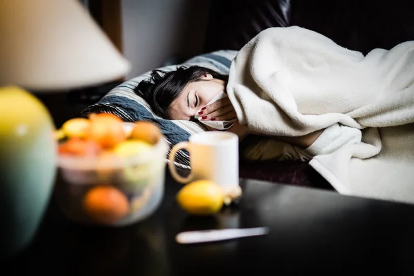 Sick woman in bed,calling in sick,day off from work.Thermometer to check temperature for fever.Vitamins and hot tea in front.Flu.Woman Caught Cold.Virus.Sick woman laying in bed under wool blanket — Stock fotografie