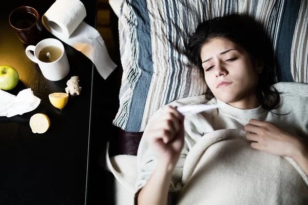 Mujer joven enferma en la cama en casa teniendo gripe, midiendo la temperatura.Termómetro para comprobar la temperatura para la fiebre.Flu.Virus.Mujer enferma acostada en la cama.Enfoque en el termómetro — Foto de Stock