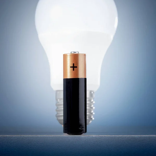 Energy efficient battery and light bulb on blue background. Electricity renewable energy concept.