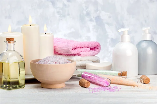 Spa cosmetics products, lotion, cream, bath salt, essential oil, soap, towels on wooden shelf.