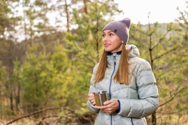 Mutlu genç bayan çay içiyor ve sonbahar ormanında eğleniyor..