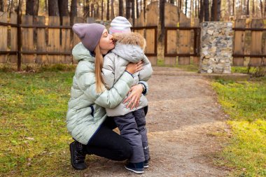 Genç bir anne, sonbahar parkında ağlayan kızını kucaklıyor, sakinleştiriyor. Ebeveynlik kavramı.
