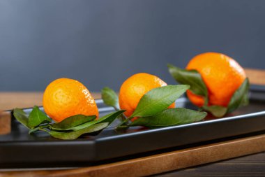 Koyu gri arka plana karşı kırsal ahşap plaka üzerinde taze mandalinalar.