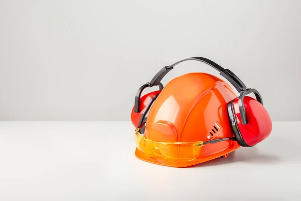 Protective helmet with headphones and glasses on gray surface with copy space.