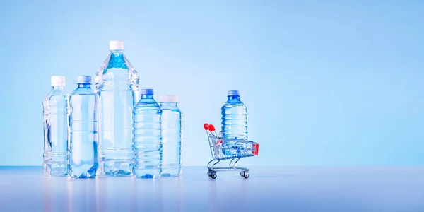 Bir şişe su alışveriş arabasında. Mavi arka planda bir grup plastik şişe ve kopya alanı var..