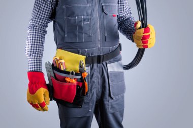 Gri arka planda kabloları olan üniformalı bir elektrikçi.. 