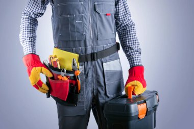 Tulumlu, gri arka planda alet çantalı bir elektrikçi. Onarım ve yenileme hizmeti kavramı.