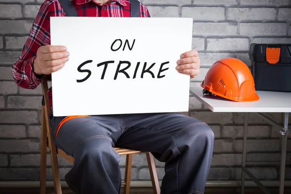 Worker on strike, builder holding poster with written protest message.