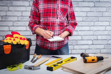 Tamirci defterde çizim yapmış. İş yerinde farklı aletleri olan bir tamirci. DIY kavramı.