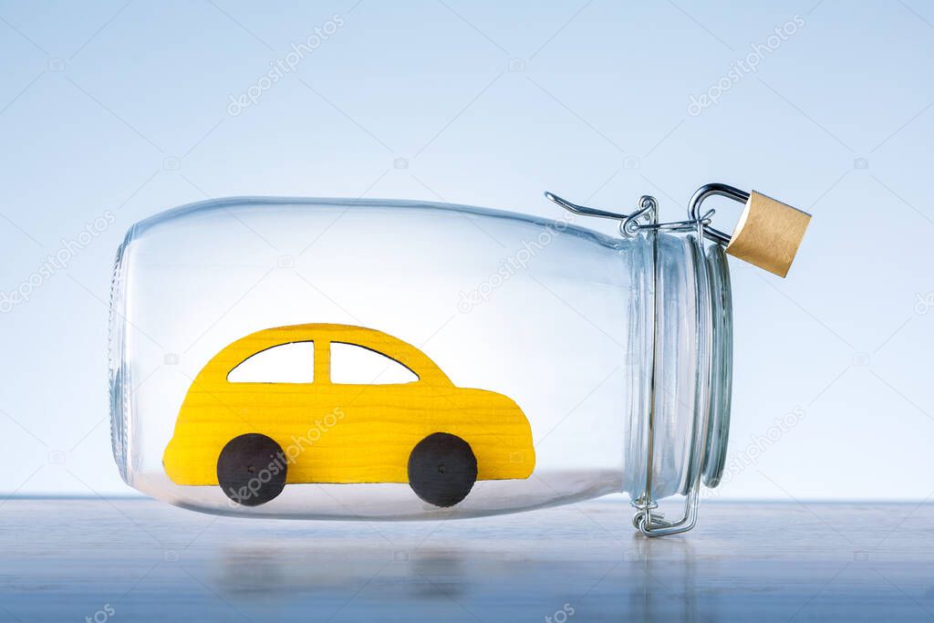 Yellow toy car protected in glass safe with lock on blue background. Car insurance concept. Safety of auto. 
