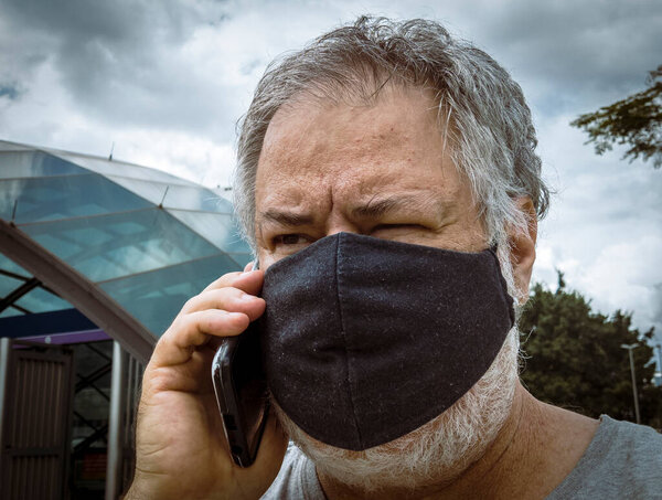 Caucasian middle age man in face mask with mobile phone in Brazil. Personal protective equipment against spread of virus. Coronavirus COVID-19 respiratory disease illness quarantine.