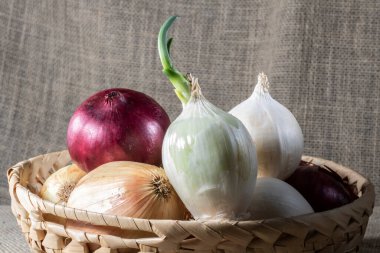 Brezilya 'da yeşim taşı arka planlı ahşap bir masada saman sepetinde farklı çeşitteki soğanlar..
