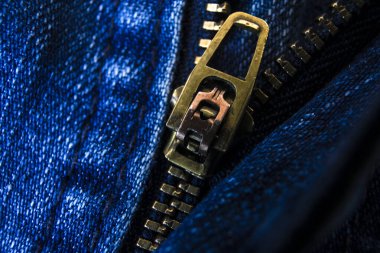 Kısmen açılmış koyu mavi kotun yakın çekimi, kumaş dokusunu ve metal detaylarını kısıtlı odak noktasıyla vurguluyor.