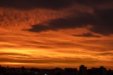 Şehrin ufuk çizgisinde dramatik ve ateşli bir turuncu gün doğumu yanar. Şehir binalarının karanlık siluetleri, canlı ve renkli gökyüzüne zıt düşerek güzel bir atmosferik manzara yaratıyor..