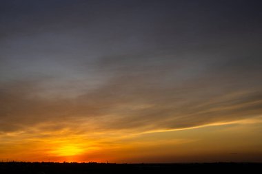Dramatik bir günbatımı, gökyüzünü turuncu ve altın sarısı renklerle, siluetli bir manzara üzerine boyar. Günün son ışığı huzurlu ve güzel bir alacakaranlık sahnesi yaratır..