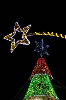 Büyük bir kayan yıldız ve karanlık gece gökyüzüne karşı renkli bir ağaç ile canlı Noel ışıkları sergilenir. Şenlikli, parıldayan tatil aydınlatması mevsimsel kutlama ve tasarım kavramları için mükemmel..