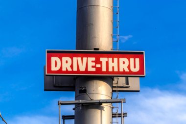 Açık mavi gökyüzüne karşı büyük metal bir direkte kırmızı ve beyaz bir açık hava levhası sergilenir. Bu evrensel kabul görmüş sembol kolaylığı, hızlı hizmeti ve modern tüketici kültürünü temsil etmektedir..