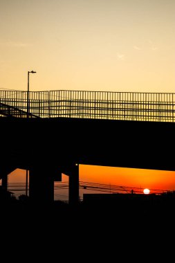 Köprüden görülen çarpıcı bir günbatımı siluettir. Bu görüntü, çevre ve mimari ile ilgili materyaller için mükemmel olan kentsel altyapının sakin etkileşimini yakalar..