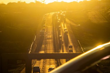 Marilia, SP, Brezilya, 19 Kasım 2025. Marilia 'da gün batımında SP-294 otoyolu. Araç ve kamyonların yoğun trafiği, altın saat ışığıyla aydınlatılan yeşil arazide akıyor..