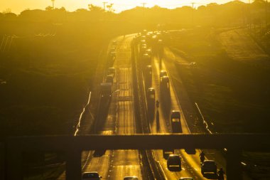 Marilia, SP, Brezilya, 19 Kasım 2025. Marilia 'da gün batımında SP-294 otoyolu. Araç ve kamyonların yoğun trafiği, altın saat ışığıyla aydınlatılan yeşil arazide akıyor..