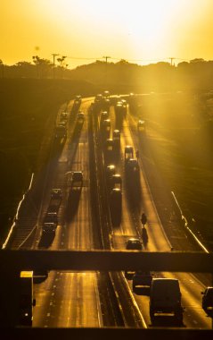 Marilia, SP, Brezilya, 19 Kasım 2025. Marilia 'da gün batımında SP-294 otoyolu. Araç ve kamyonların yoğun trafiği, altın saat ışığıyla aydınlatılan yeşil arazide akıyor..