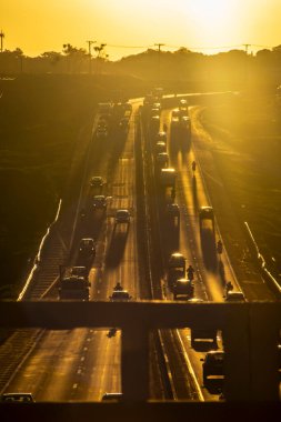 Marilia, SP, Brezilya, 19 Kasım 2025. Marilia 'da gün batımında SP-294 otoyolu. Araç ve kamyonların yoğun trafiği, altın saat ışığıyla aydınlatılan yeşil arazide akıyor..