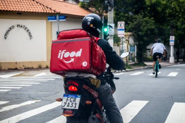 Sao Paulo, Brezilya, 19 Aralık 2025. Motosikletli bir dağıtım uygulaması Sao Paulo 'da trafik ışığında bekliyor. Görüntü, konser ekonomisi ve modern şehir yaşamını gözler önüne seriyor.