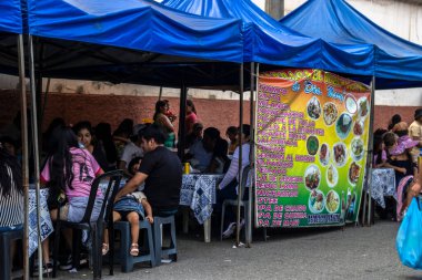 Sao Paulo, Brezilya, 12 / 21 / 2025. Sao Paulo 'daki Bolivya sokak gıda pazarı. İnsanlar Thimpu ve Lechon al Horno gibi geleneksel And yemeklerini yemek için mavi çadırların altında toplanıyor..