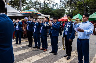 Sao Paulo, Brezilya, 12 / 21 / 2025. Bando, Kantuta Meydanı 'nda konser veriyor. Mavi üniformalı müzisyenler, bir Bolivya sokak fuarı sırasında zengin kültürel çeşitliliği yansıtan rüzgar enstrümanları çalıyorlar.