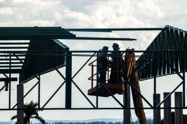 Marilia, Sao Paulo, Brezilya, 16 Şubat 2026. Siluetli inşaat işçileri, Brezilya 'da bulutlu bir gökyüzüne karşı ağır çelik yapı iskeleti oluşturmak için havadan yükseltici kullanıyorlar. İnşaat işçileri bunun için metal bir yapı oluşturuyorlar.