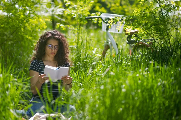 Preciosa joven morena, leyendo un libro en un parque — Foto de Stock