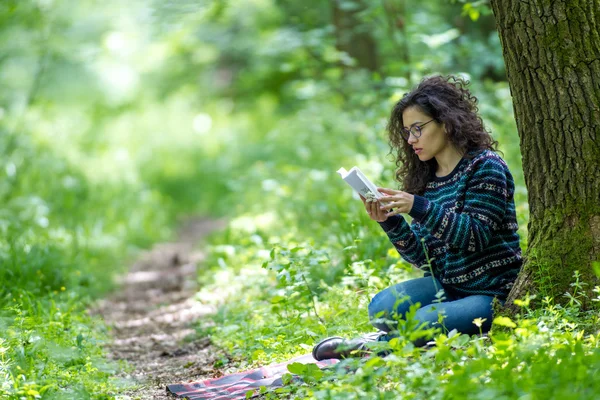 Belle jeune femme brune, lisant un livre dans un parc — Photo