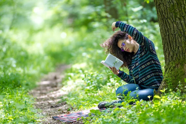 Belle jeune femme brune, lisant un livre dans un parc — Photo