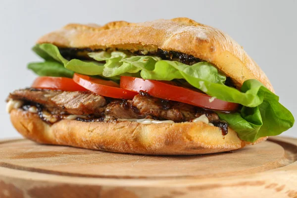 Вкусный сэндвич со свининой в чиабатте с помидорами, салатом — стоковое фото